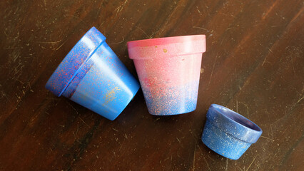 Colorful terracotta pots painted in blue and pink arylic paints. On a wooden surface. 