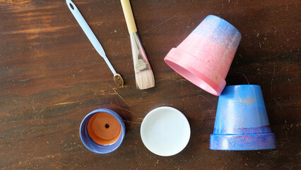 Flat lay of painted terracotta pots, paintbrush, toothbrush and a paint tray. On a wooden surface.