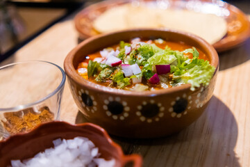 Clay bowl of delicious and traditional Mexican pozole on wooden table