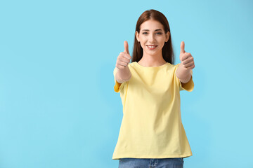 Young woman in modern t-shirt showing thumb-up on color background