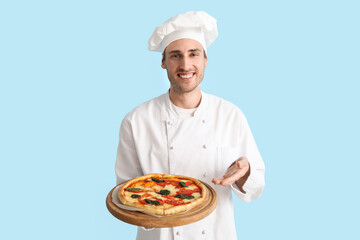 Handsome chef showing tasty pizza on blue background