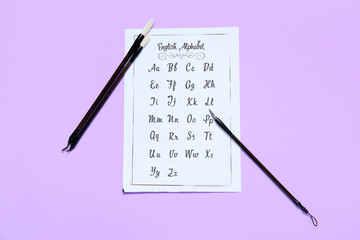 Paper with alphabet and brushes on lilac background