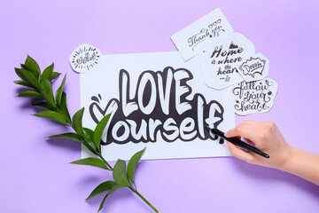Woman writing text LOVE YOURSELF on lilac background