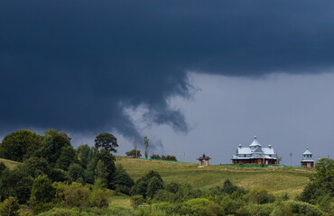 Storm clouds, ominous sky, hill and church, green trees before the rain