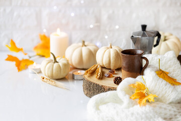 Cozy Fall setting with a cup of espresso coffee in a rustic cup, moka pot at the background with white pumpkins, autumnal leaves and burning candles.