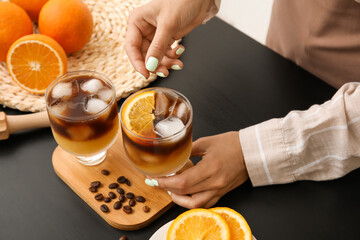 Woman holding glass of tasty coffee with orange juice on table, closeup
