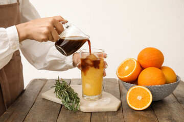 Woman pouring coffee into glass with orange juice on light background, closeup