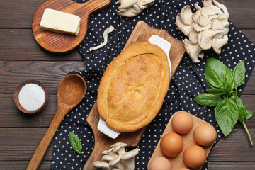 Baking dish with tasty mushroom pot pie and ingredients on black wooden background