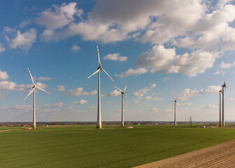 Aerial view of large wind turbines with blades in field against blue sky and white clouds. Alternative energy. Wind farm generating green energy.
