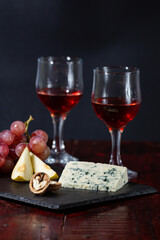 Wine, cheese, some grapes and pear on wooden plate on black background