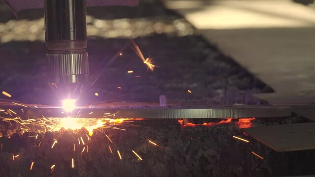 Close-up demonstration of industrial plasma laser cutting. Electric computer operated system in metalworking industry. Automated laser-cutter burns metal sheet and plates with spark flying around.