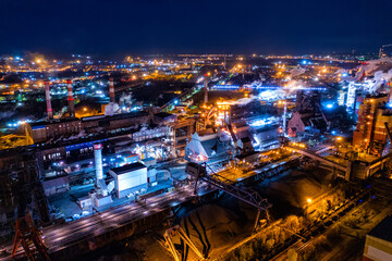 Aerial view of steel plant at night with smokestacks and fire blazing out of the pipe. Industrial panoramic landmark with blast furnance of metallurgical production. Concept of environmental pollution