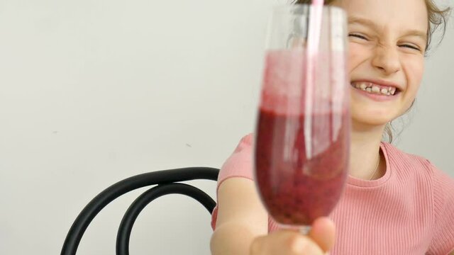 Sweet little girl drinks raspberry smoothie and smiles. Vegetarian drink. Close-up portrait of a child who enjoys a refreshing tasty raspberry juice, healthy eating