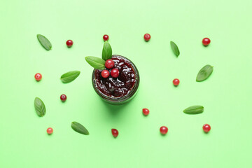 Glass jar with tasty cranberry jam on green background