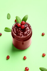 Glass jar with tasty cranberry jam on green background