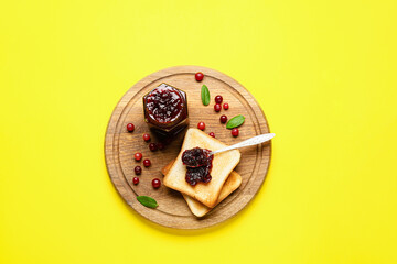 Wooden board with tasty toasts and cranberry jam on yellow background