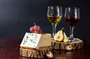 Wine, cheese, some grapes and pear on wooden plate on black background