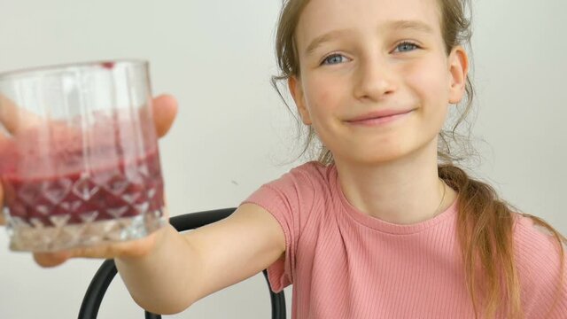 Sweet little girl drinks raspberry smoothie and smiles. Vegetarian drink. Close-up portrait of a child who enjoys a refreshing tasty raspberry juice, healthy eating