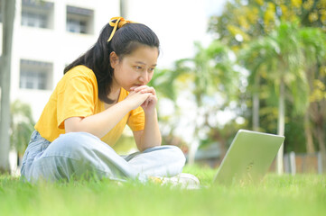 Teenager girl sitting on the lawn looking at laptop, work from home.