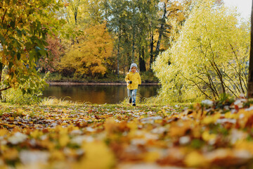 happy smiling little boy in yellow jacket run in autumn central park in Saint-petersburg, Russia on...