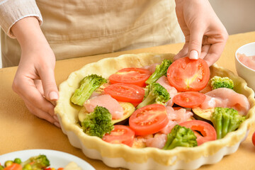 Woman preparing chicken pot pie with vegetables at kitchen table, closeup
