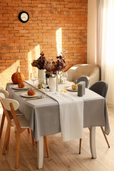 Dining table with pumpkins and flowers near brick wall