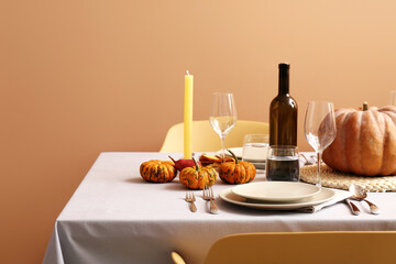 Autumn table setting with fresh pumpkins and candles near beige wall