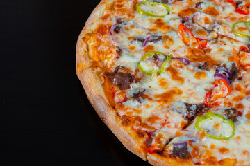 Slice of pizza with meat and vegetables on a black background
