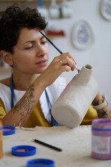 Professional ceramist painting pottery during master class lesson in workshop. Creative craftswoman...