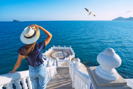 Carefree young tourist woman in sun hat enjoying sea view at Balcon del Mediterraneo in Benidorm, Spain. Summer vacation in Spain