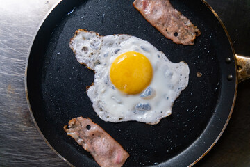 Delicious fried egg and bacon strips on a frying pan