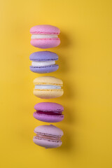 Colorful composition of different varieties of macoron cookies on yellow background.