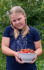 The girl holds a ripe juicy red fragrant strawberry in her hands.