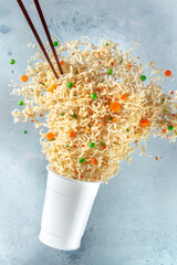 Ramen cup with noodles floating out of it and chopsticks, fast food levitation. Instant noodle meal...