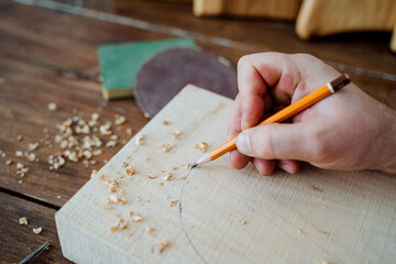 The carpenter draws with a pencil on the board. hand holds a pencil, carpentry workshop, sketch of the future product