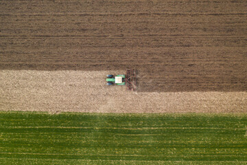 Fototapeta na wymiar Aerial view of agricultural tractor tilling and harrowing ploughed field, directly above drone pov