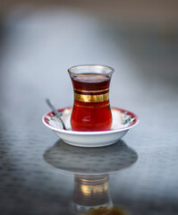 herbal black tea in a traditional tea cup and saucer with teaspoon, on a reflective glass table outdoors