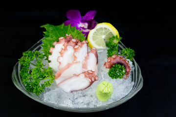 Octopus tentacles in a bowl over ice served with wasabi and oba leaves, lemon