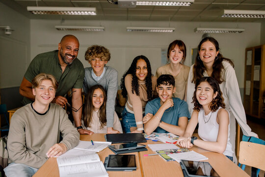 Portrait of smiling teenage girls and boys with male professor in classroom