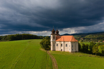 Fototapeta premium Church of St. Margaret from the 18th century near Šonov. Beautiful church chapel in middle of fields in czech countryside broumovsko region with hills of broumov walls on background. Aerial view 