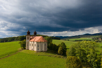 Fototapeta na wymiar Church of St. Margaret from the 18th century near Šonov. Beautiful church chapel in middle of fields in czech countryside broumovsko region with hills of broumov walls on background. Aerial view 