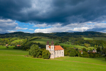 Fototapeta premium Church of St. Margaret from the 18th century near Šonov. Beautiful church chapel in middle of fields in czech countryside broumovsko region with hills of broumov walls on background. Aerial view 