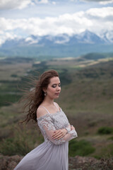 A beautiful girl in a gray dress walks against the backdrop of a mountain range. Wind in your hair. Kurai steppe. Severo-Chuisky Khrbet. Altai mountains. Photoshoot in a fairy-tale style.