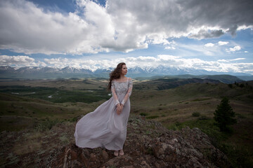 A beautiful girl in a gray dress walks against the backdrop of a mountain range. Wind in your hair....