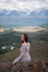 Fototapeta na wymiar A beautiful girl in a gray dress walks against the backdrop of a mountain range. Wind in your hair. Kurai steppe. Severo-Chuisky Khrbet. Altai mountains. Photoshoot in a fairy-tale style.
