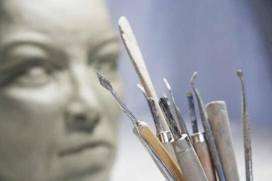 Artistic sculpting tools, blurred face in clay in the background