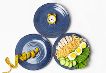Plates with food, alarm clock and measuring tape, intermittent fasting concept.