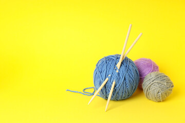 Multi-colored balls of yarn with knitting needles on yellow background