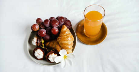 Breakfast, fruit, croissants, orange juice on a white bedsheet, Healthy food concept