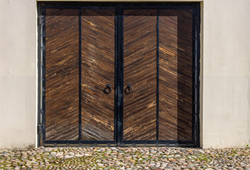 Large vintage wooden gate wrought iron in a light stone wall. There is an old stone pavement in front of the gate.